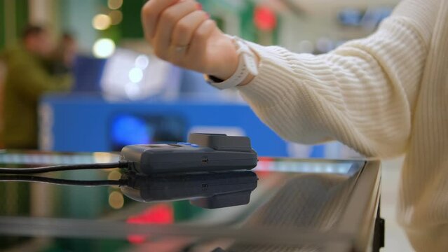 Wireless payment by smart watch using e wallet on pos terminal or card reader. Female buyer hand pays electronic cashless money at shopping place close up indoors