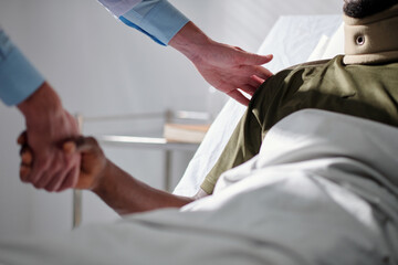 Close-up of doctor shaking hands with patient and supporting him while he lying on bed in hospital