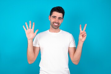 Young man standing over blue studio background showing and pointing up with fingers number seven...