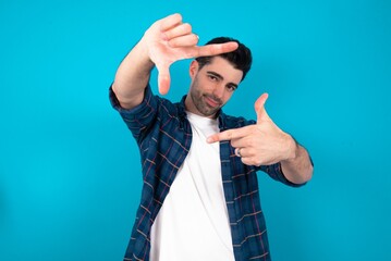 Naklejka premium Young man standing over blue studio background making finger frame with hands. Creativity and photography concept.