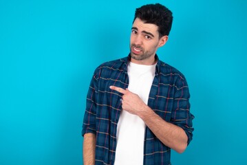 Young man standing over blue studio background Pointing aside worried and nervous with forefinger, concern and surprise concept.