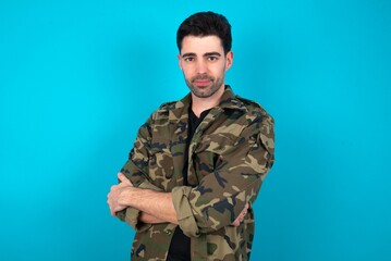 Portrait of Young man standing over blue studio background standing with folded arms and smiling