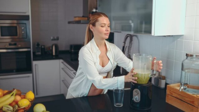 A young pregnant woman is preparing a smoothie with a blender in the kitchen. A pregnant woman drinks a vitamin smoothie. The concept of healthy eating during pregnancy.