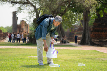 senior male tourist picking up plastic bottles on the grass left by tourists in a historical park,concept raising awareness of saving the world and reducing global warming