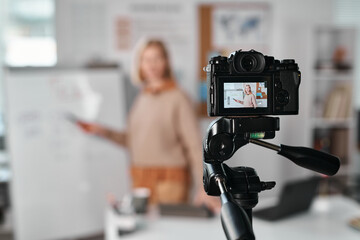 Mature teacher standing near the whiteboard in front of professional camera and recording lesson online