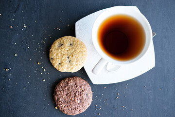 Obraz na płótnie Canvas Two cookies with a cup of black tea on black background, brown cookies with afternoon tea concept.
