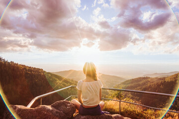 Frau meditiert auf Felsen mit Bergblick, Talblick und Gegenlicht vom Sonnenuntergang, umgeben von...