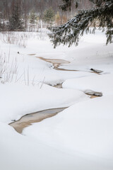 a small melting stream flow in snow covered winter forest landscape
