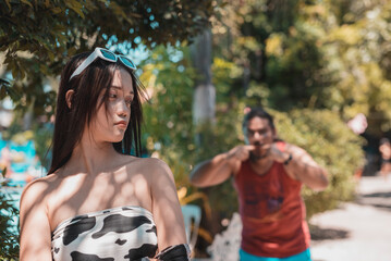 A young woman being harassed by an older man catcalling and stalking her while at a public resort.