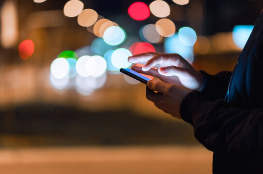 Close-up shot of an unrecognizable man using a phone in the city at night.