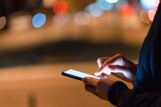 Close-up shot of an unrecognizable man using a phone in the city at night. Blank screen.