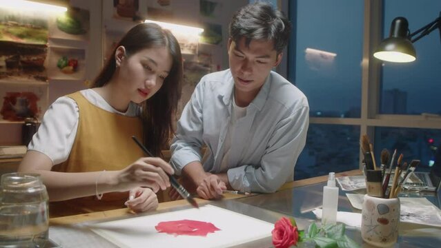 Zoom out shot of young Asian painting picture together with male teacher while attending class in art school