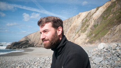 Hombre barbudo sentado en una playa rocosa