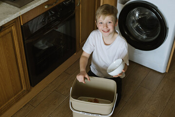 Boy In Kitchen Making Compost Scraping Vegetable Leftovers Into Bin