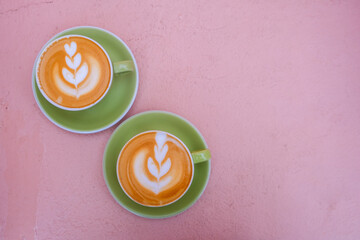Two green cups of cappuccino with latte art on pink pastel backround