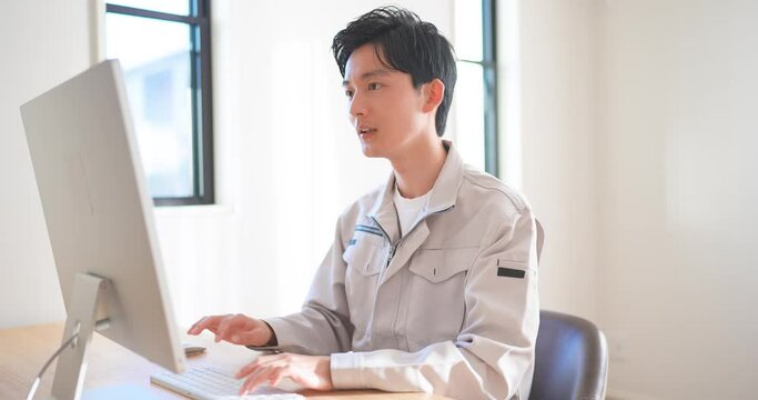 作業着を着てパソコン作業をする若いエンジニアの男性