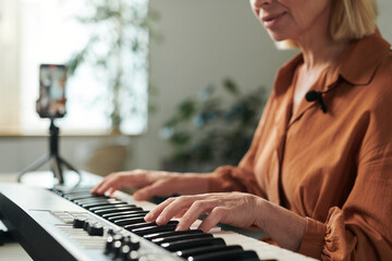 Mature teacher playing on piano online and recording her lesson on professional camera for students