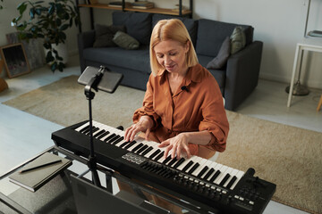 Mature woman having musical lesson with her student online, she sitting at table and playing piano