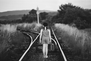 A little girl in a dress walking on an abandoned railroad tracks.