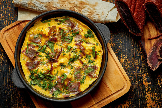 Menemen with eggs, Sujuk, green peppers, and spices served with bread in pan. Turkish breakfast