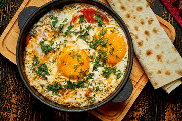 Fried eggs with tomatoes, onions and pita bread in a pan on a wooden background. Tasty Shakshuka