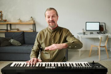Portrait of mature teacher teaching to play piano online while sitting in the room at home