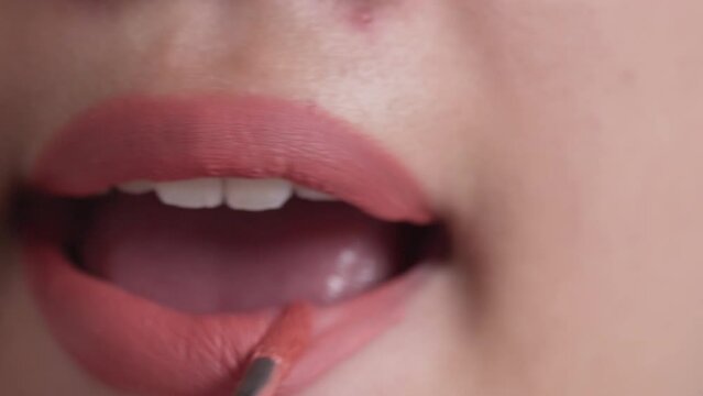 Closeup shot of woman paints her lips with lipstick.
