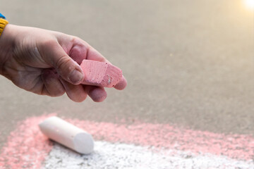 a piece of colored chalk in the hand of a child on the street. soft focus
