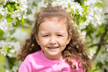 portrait happy little beautiful cute girl smelling flowers of blossoming apple tree. concept of spring mood child, summer. baby summer time