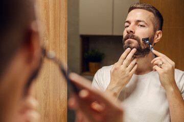 Reflection of a man shaving his beard with razor blade.
