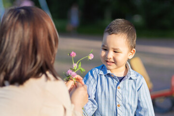 happy boy giving mom a flower. Asian kid presenting for mother bouquet of wildflowers clover. Mothers day celebration concept. Kazakh family together. Woman and child daylight saving time