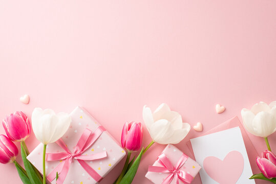 Mother's Day celebration concept. Top view photo of gift boxes with ribbon bows pink and white tulips envelope with letter and small hearts on isolated pastel pink background with copyspace