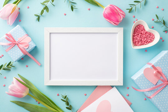 Mother's Day concept. Top view photo of photo frame tulips gift boxes envelope with postcard and heart shaped saucer with sprinkles on isolated pastel blue background with empty space