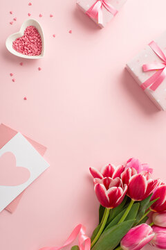 Mother's Day concept. Top view vertical photo of bouquet of tulips gift boxes envelope with postcard heart shaped saucer with sprinkles on isolated pastel pink background with copyspace in the middle
