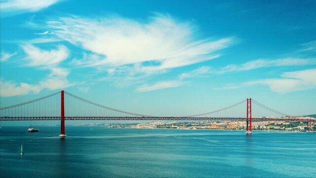 Time-lapse of 25 de Abril Bridge famous tourist landmark of Lisbon connecting Lisboa to Almada on Setubal Peninsula over Tagus river with boats yachts and vessels moving. Lisbon, Portugal