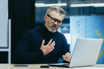 businessman heart attack at workplace, mature gray haired man working on laptop has severe chest pain heartache, senior boss in glasses.