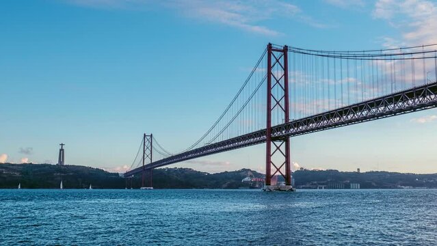 Time-lapse of 25 de Abril Bridge famous tourist landmark of Lisbon connecting Lisboa to Almada on Setubal Peninsula over Tagus river with tourist yacht boats passing under. Lisbon, Portugal