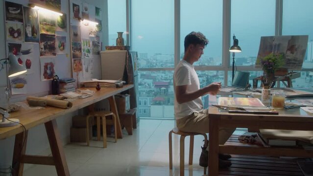 Full shot with copy space of professional male artist painting picture at workplace in creative studio with panoramic windows