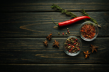 A set of peppers for adding to food and dry spices. Red chili pepper pods and dry star anise on black vintage kitchen table - obrazy, fototapety, plakaty