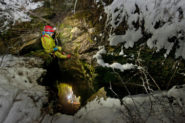 Female caver explorer entering a cave in the mountains. © Milos
