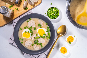 White Eastern European borscht. Traditional Polish white soup Zurek, with sausages, egg, herbs and green onions