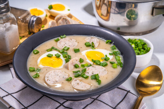 White Eastern European borscht. Traditional Polish white soup Zurek, with sausages, egg, herbs and green onions