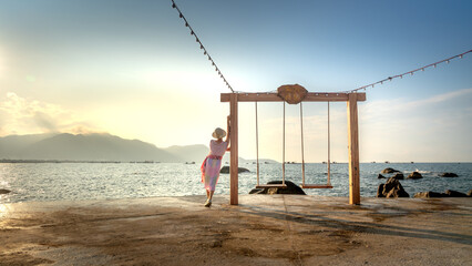 A female tourist relaxes on a swing at a tropical beach at 4-star Hon Co Resort, Ca Na in Ninh province. Thuan, Vietnam. She feels comfortable and happy with the scenery here