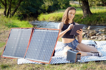 Woman uses solar panel and power station outdoors on camping to generate electricity for tablet pc or smartphone