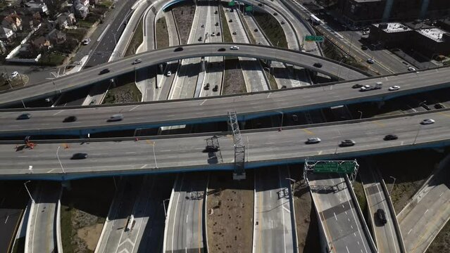 An aerial view high over a highway intersection in Queens, New York on a sunny day. The drone camera tilted downwards, dolly in over the complicated interchange.