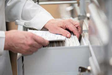 The nurse's hands are looking in the archive for a patient's card. The file is in a cell in the clinic.