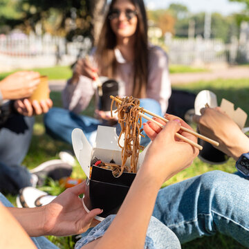 Friends young girls, girlfriends sit cute outdoors in nature, takeaway food, takeaway paper box.