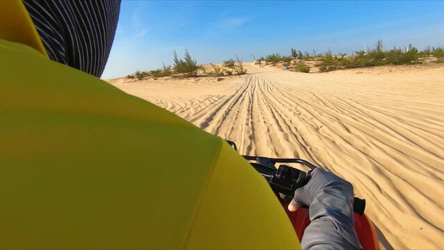 Tourist riding quad bike up massive sand dune in day; FPV view