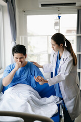 Fototapeta premium Doctor and young male patient who lie on the bed while checking pulse, consult and explain with nurse taking note in hospital
