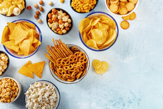 Salty snacks, party mix, shot from the top with copy space. An assortment of appetizers, a flat lay on a slate background. Potato and tortilla chips, crackers, popcorn etc